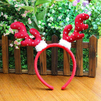 Red Christmas head buckle with polka dot antlers on wooden surface with green plants background