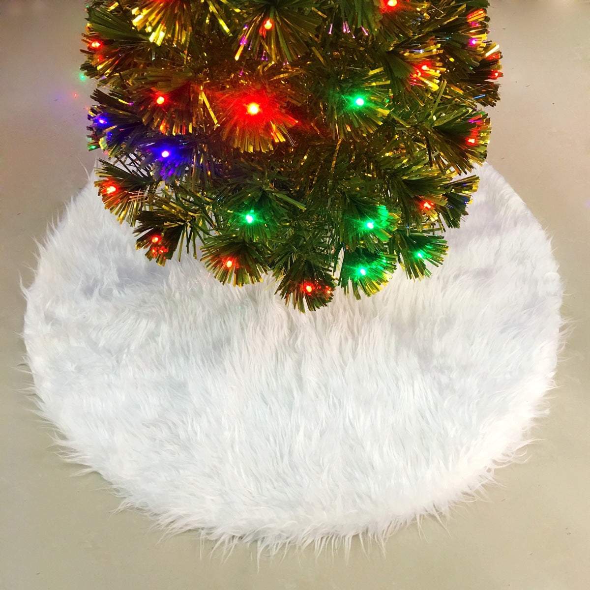 White fluffy Christmas tree skirt under decorated tree with colorful lights