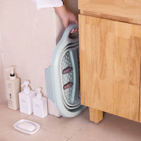 Foldable footbath massage bucket in compact design hanging by wooden cabinet in bathroom corner
