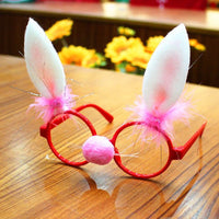 Christmas glasses frame with red round rims, pink bunny ears, and a pink nose decoration on wooden surface