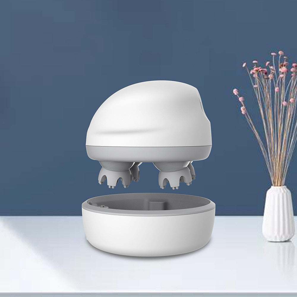 Compact white handheld head massager with kneading scalp nodes and charging base on table