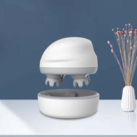 Compact white handheld head massager with kneading scalp nodes and charging base on table
