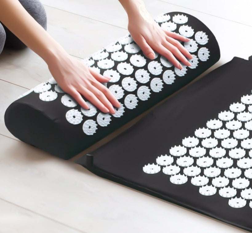 Acupuncture massage mat and pillow with white acupressure spikes on black surface for stress and pain relief