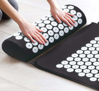 Acupuncture massage mat and pillow with white acupressure spikes on black surface for stress and pain relief